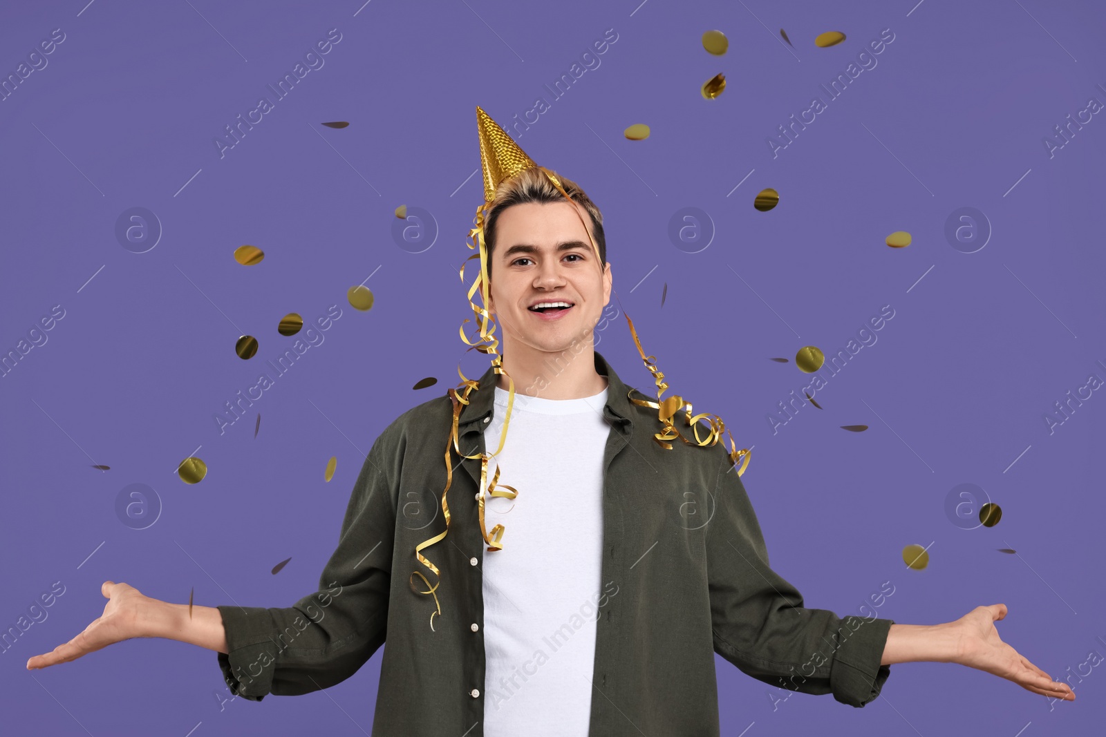 Photo of Young man with party hat and confetti on purple background