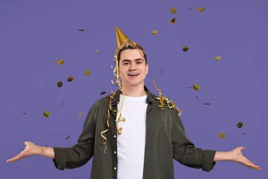 Photo of Young man with party hat and confetti on purple background