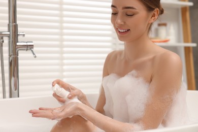 Woman applying shower gel onto hand in bath indoors