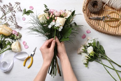 Photo of Florist making beautiful bouquet with roses at white table, top view