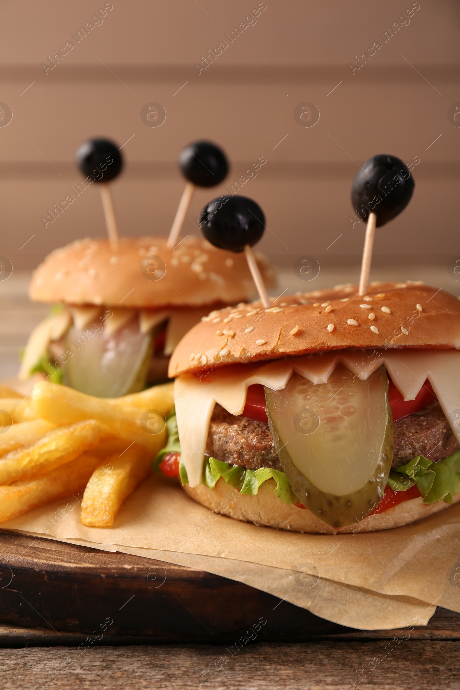 Photo of Cute monster burgers served with french fries on wooden table, closeup. Halloween party food