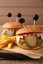 Cute monster burgers served with french fries on wooden table, closeup. Halloween party food