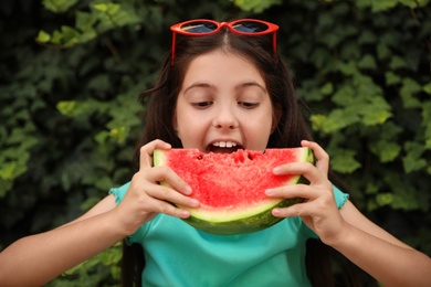 Photo of Cute little girl eating watermelon outdoors on sunny day