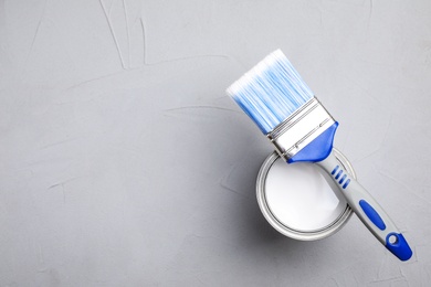 Open can with white paint and brush on grey background, top view. Space for text