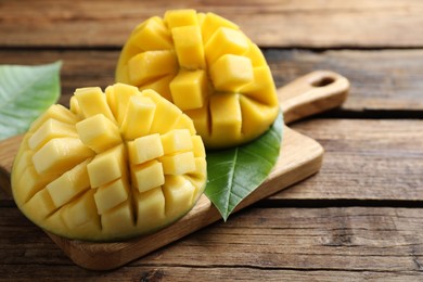 Photo of Halves of ripe mango cut into cubes on wooden table