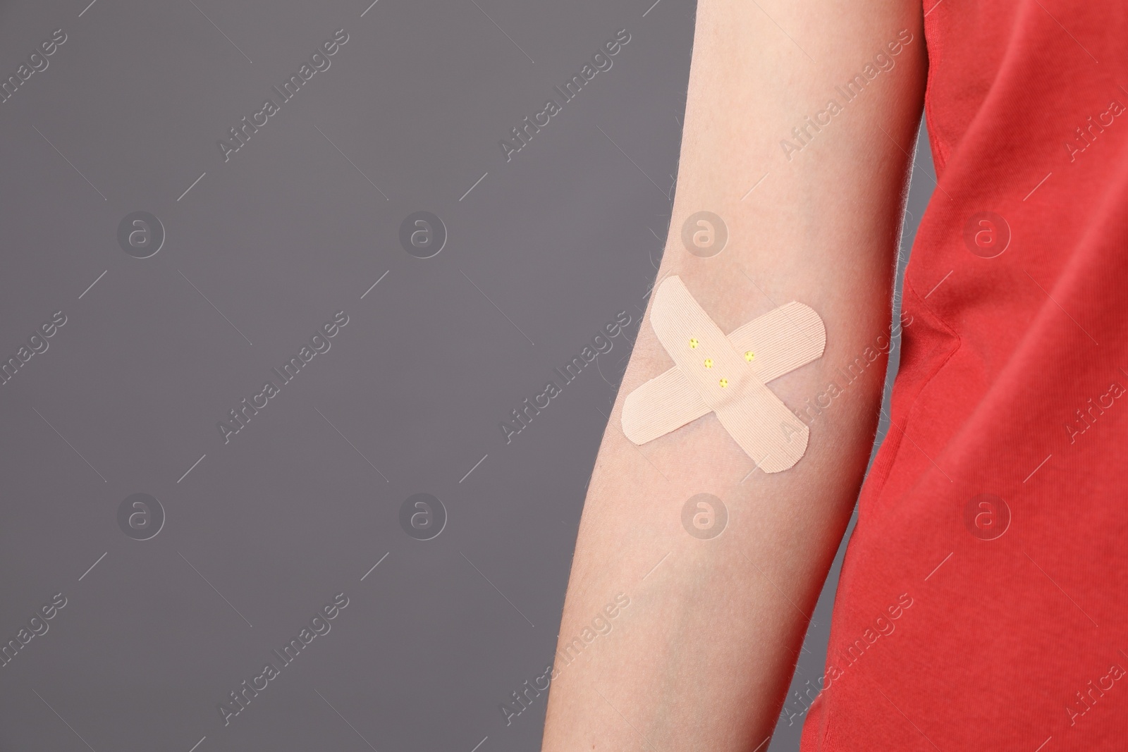 Photo of Blood donation. Woman with sticking plaster on her arm against grey background, closeup. Space for text
