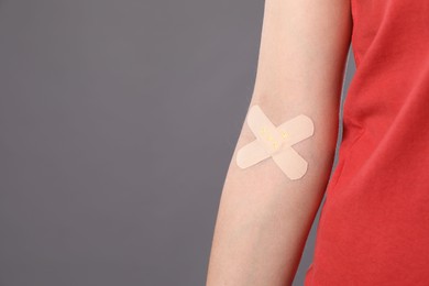 Blood donation. Woman with sticking plaster on her arm against grey background, closeup. Space for text