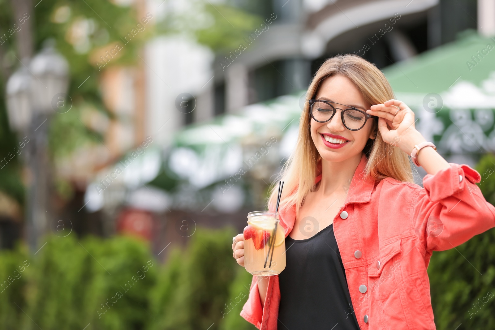 Photo of Young woman with mason jar of tasty lemonade outdoors