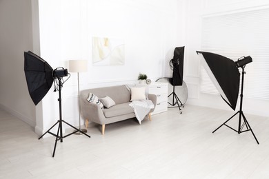 Photo of Set of stylish furniture surrounded by professional lighting equipment in photo studio. Cozy living room interior imitation