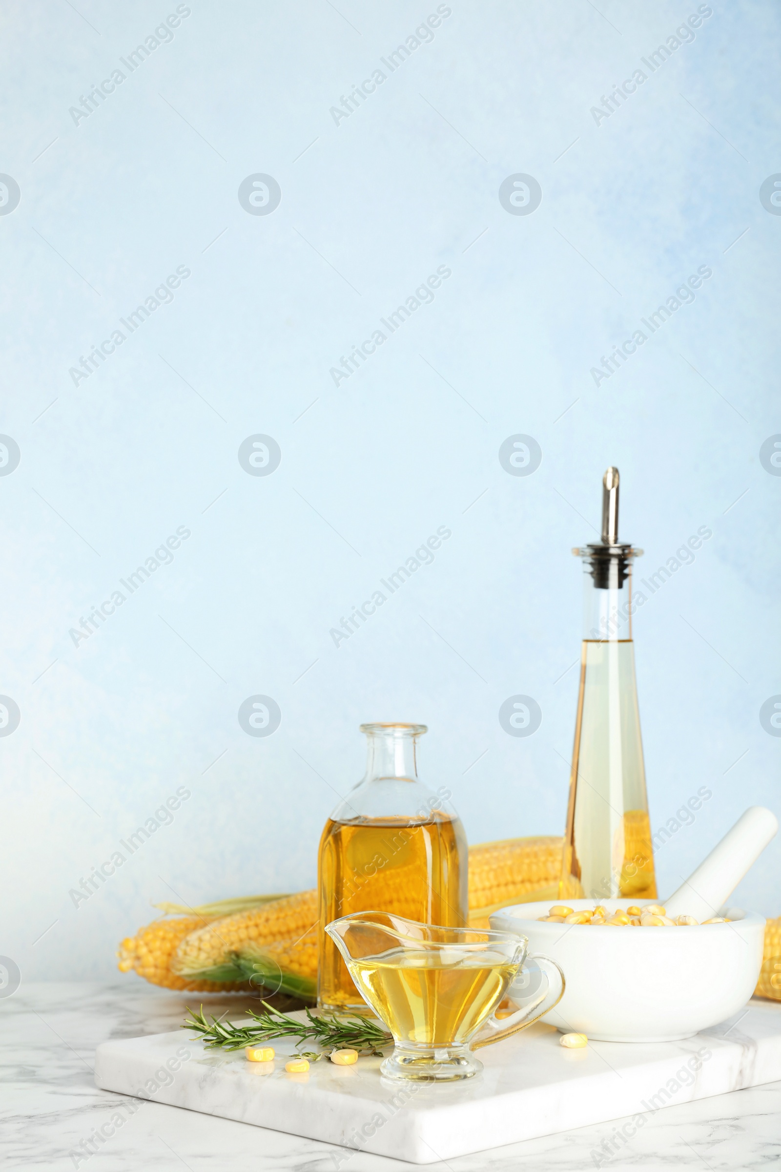 Photo of Bottles and gravy boat with fresh corn oil on table against color wall