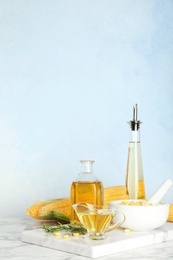 Photo of Bottles and gravy boat with fresh corn oil on table against color wall