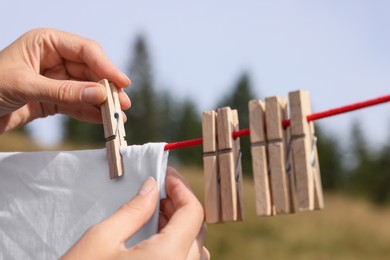 Photo of Woman hanging clean laundry with clothespins on washing line outdoors, closeup