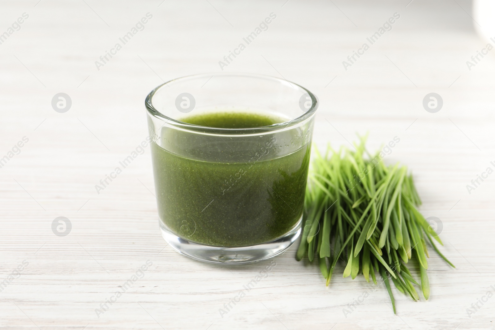 Photo of Wheat grass drink in glass and fresh sprouts on white wooden table, closeup