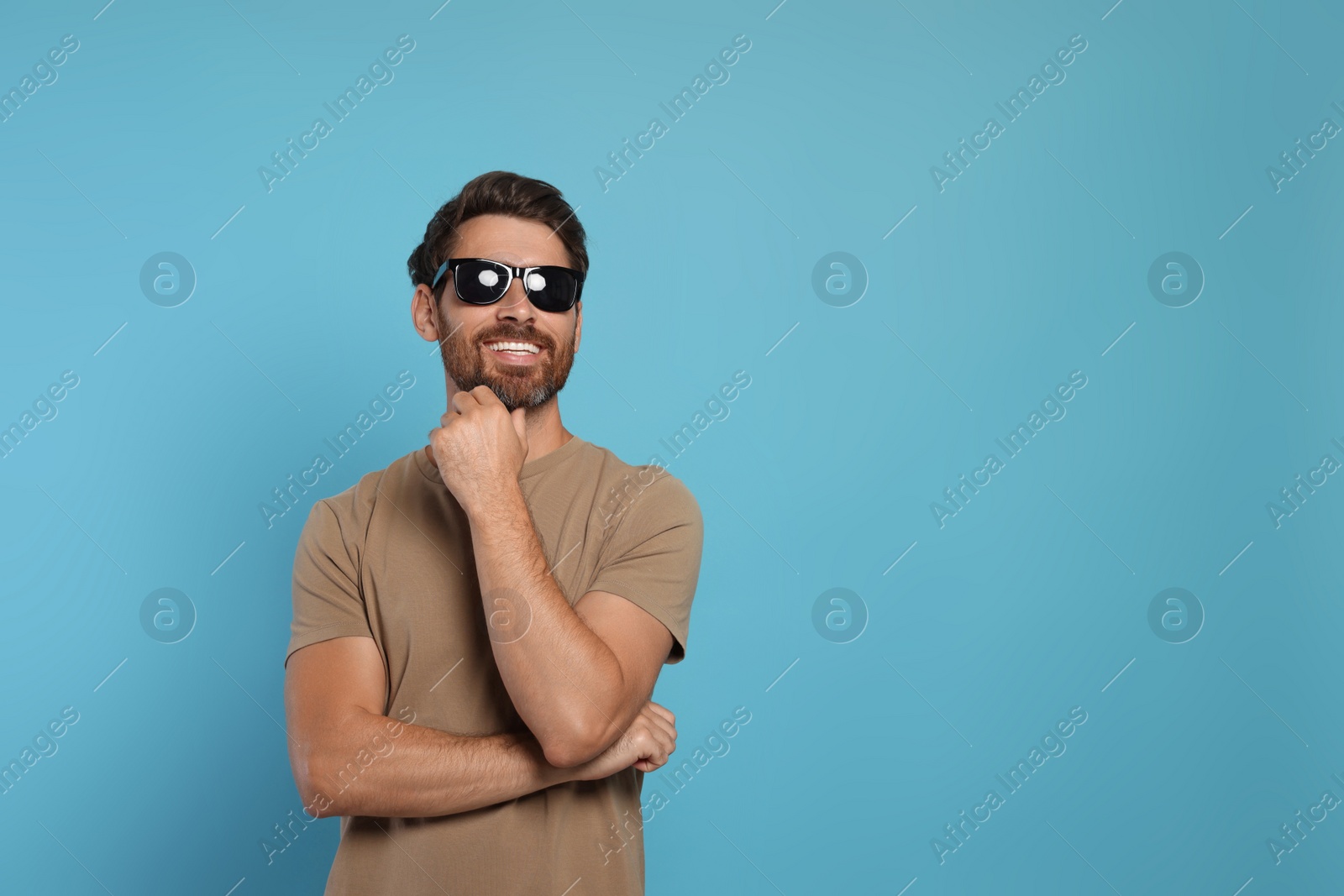 Photo of Portrait of smiling bearded man with stylish sunglasses on light blue background. Space for text