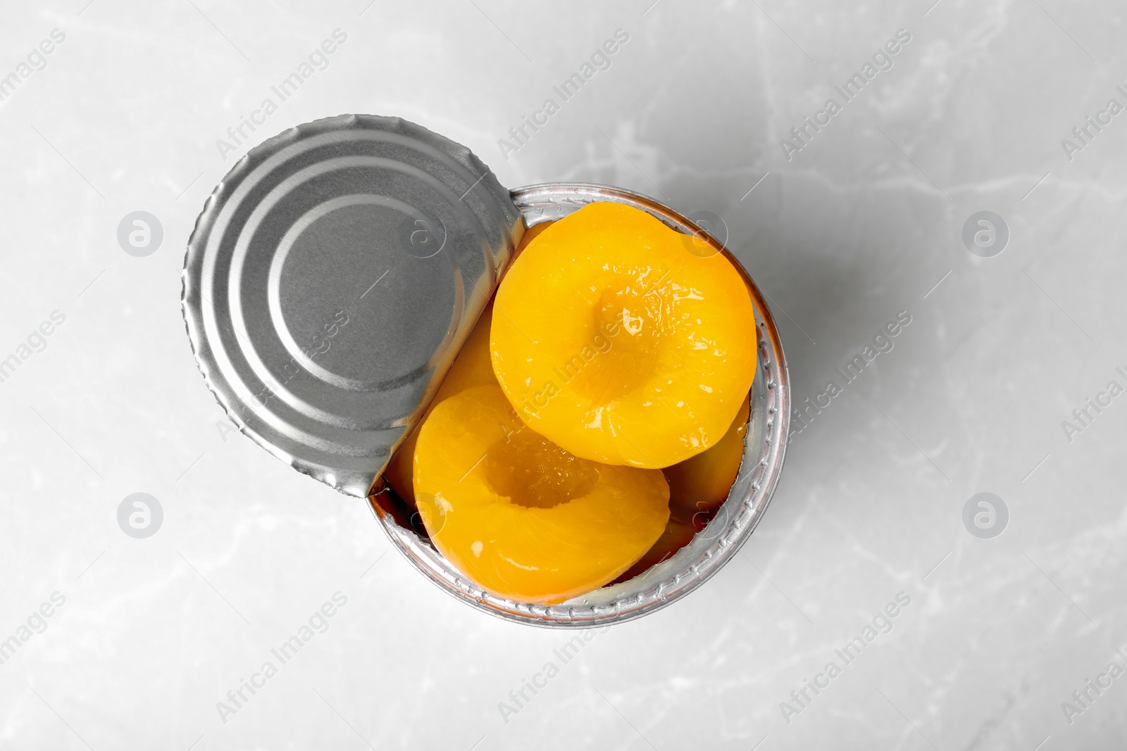 Photo of Tin can with conserved peaches on light background, top view