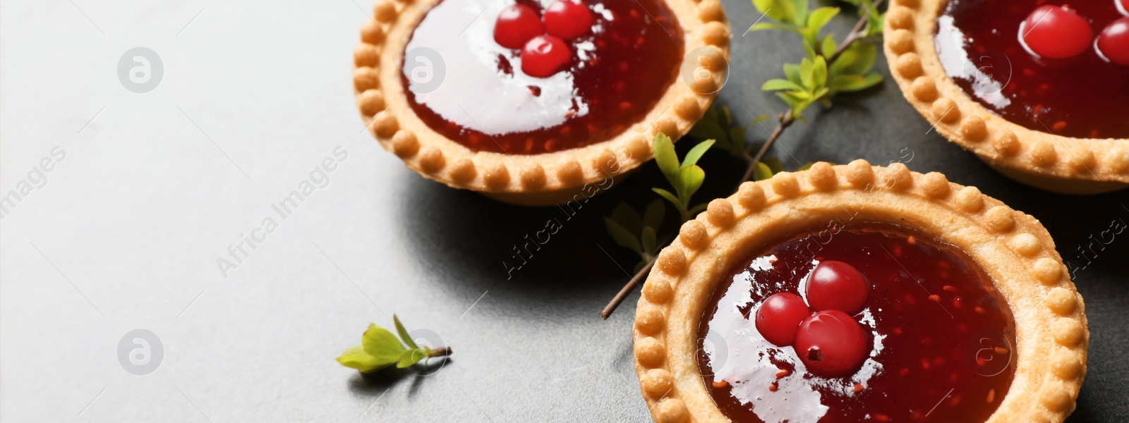 Image of Tasty tartlets with jam on grey table, closeup view with space for text. Banner design