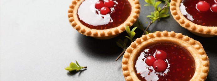 Tasty tartlets with jam on grey table, closeup view with space for text. Banner design