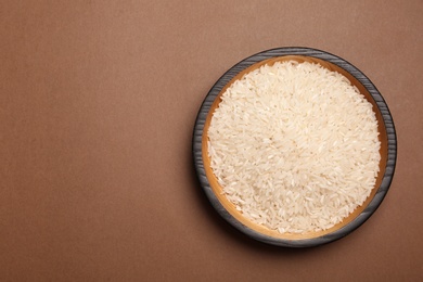 Parboiled rice in wooden bowl on color background, top view. Space for text