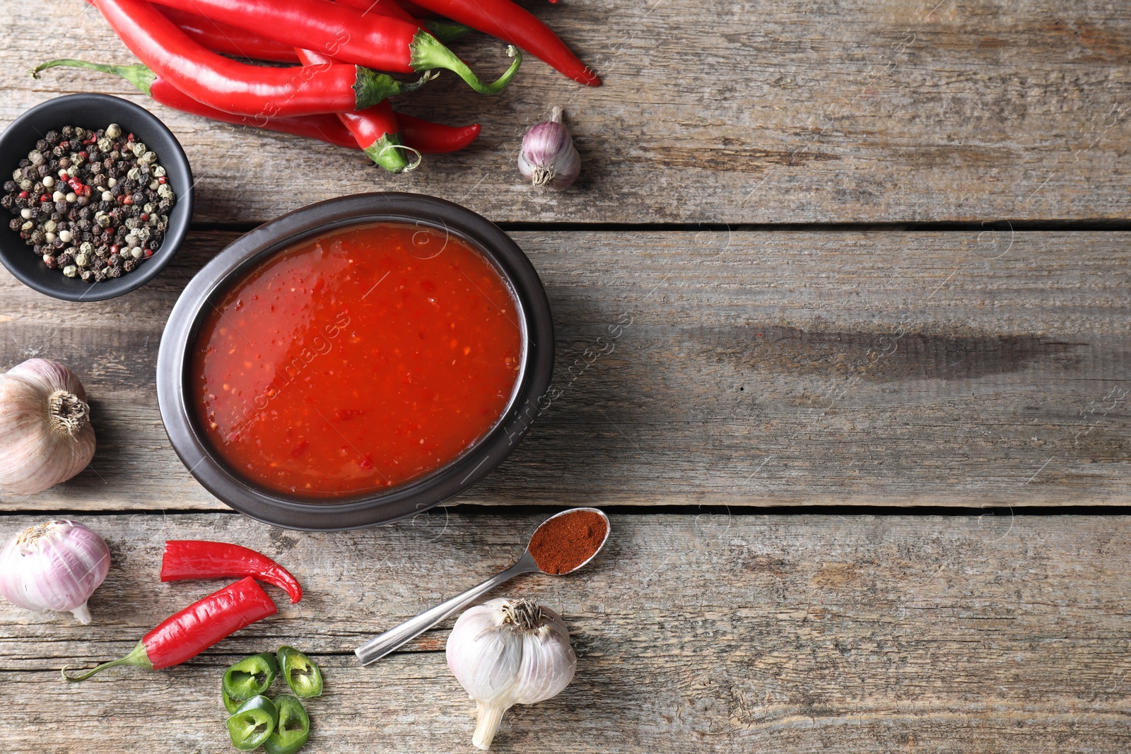 Photo of Spicy chili sauce in bowl and ingredients on wooden table, flat lay. Space for text