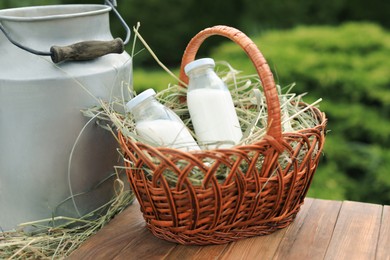 Photo of Tasty fresh milk in can and bottles on wooden table outdoors