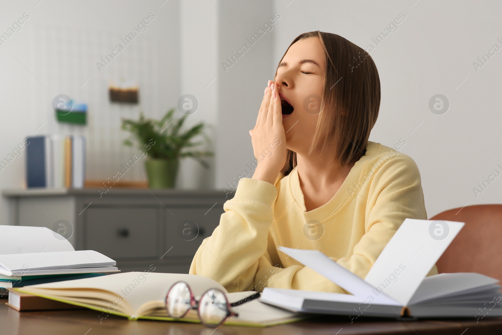 Photo of Young tired woman studying at wooden table in room