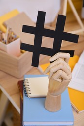 Photo of Wooden mannequin hand with paper hashtag symbol indoors