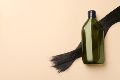 Photo of Lock of hair and shampoo bottle on beige background, flat lay. Space for text