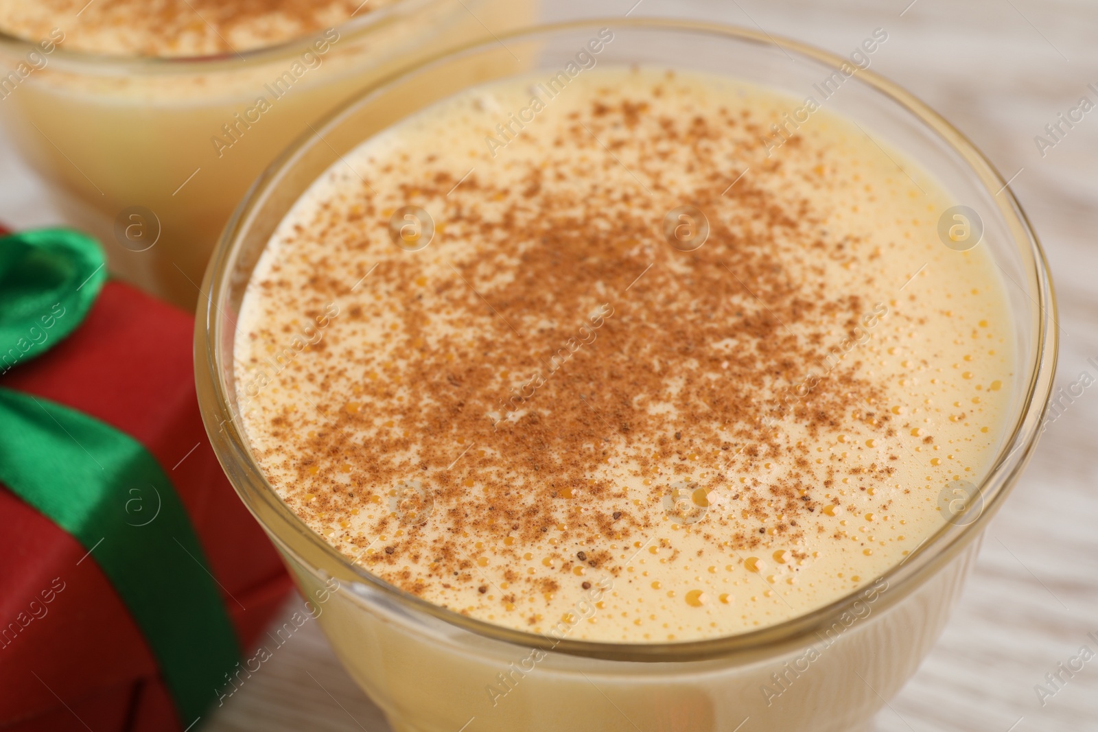 Photo of Tasty eggnog with cinnamon on white wooden table, closeup