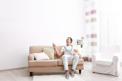 Photo of Happy young man operating air conditioner with remote control at home