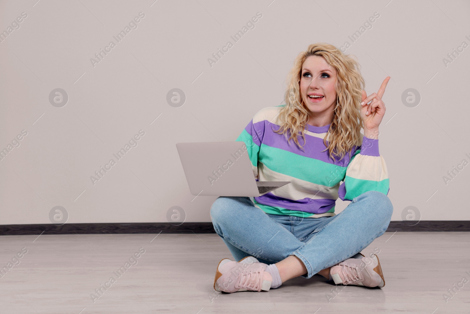 Photo of Beautiful young woman with laptop sitting on floor near grey wall. Space for text