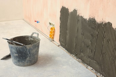 Photo of Bucket near white wall with adhesive mix for tile installation indoors