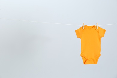 Cute baby onesie hanging on clothes line against light grey background, space for text. Laundry day