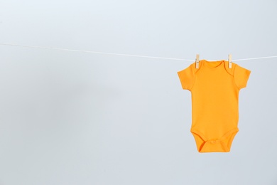 Photo of Cute baby onesie hanging on clothes line against light grey background, space for text. Laundry day