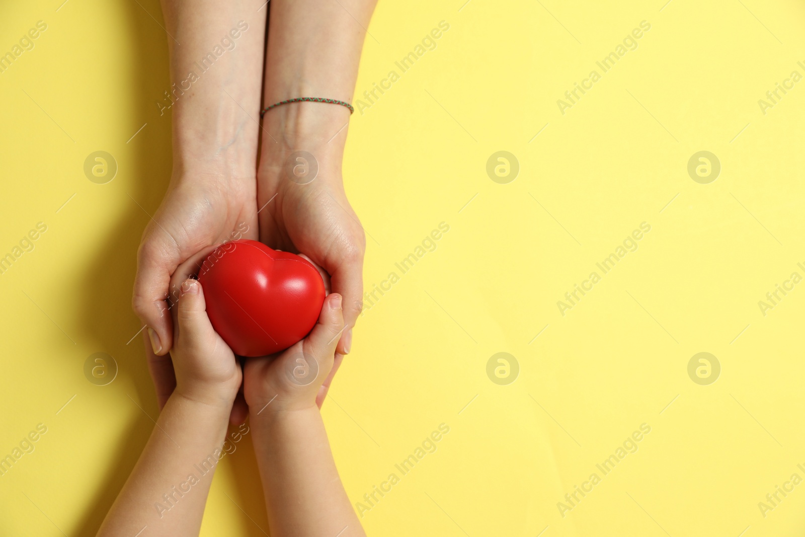 Photo of Mother and her child holding red decorative heart on pale yellow background, top view. Space for text