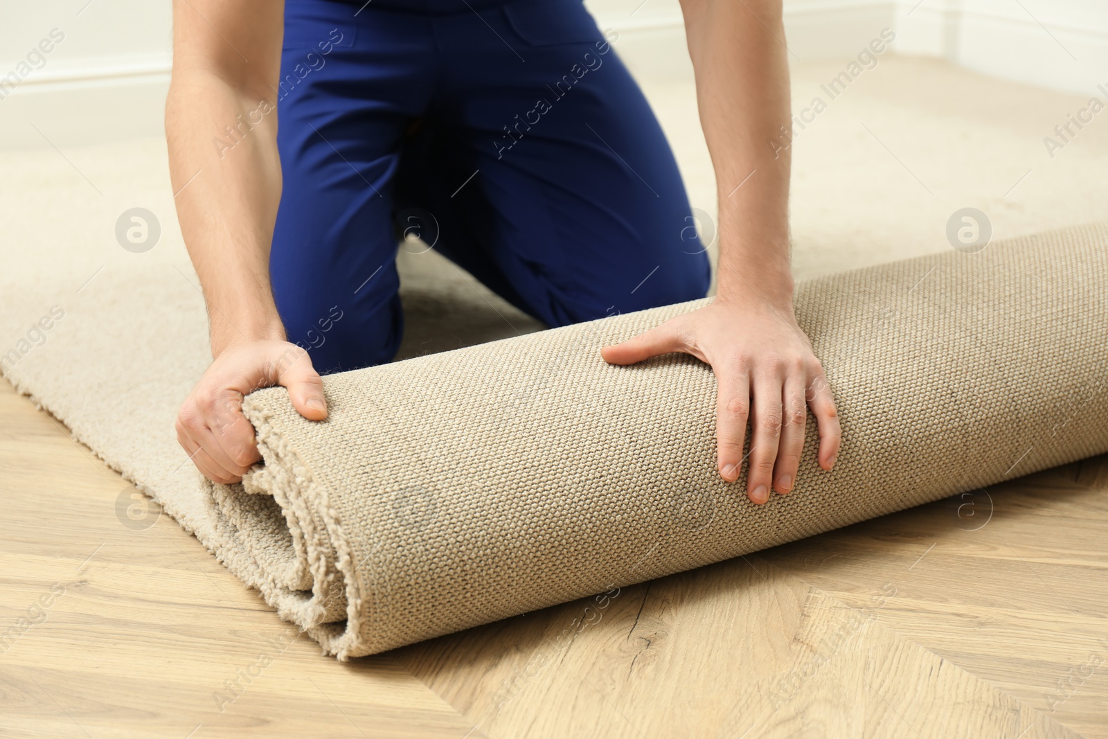 Photo of Worker rolling out new carpet flooring indoors, closeup