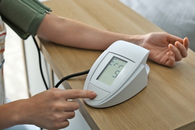 Photo of Woman checking blood pressure with sphygmomanometer at table indoors, closeup. Cardiology concept