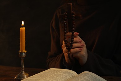 Woman praying at table with burning candle and Bible, closeup