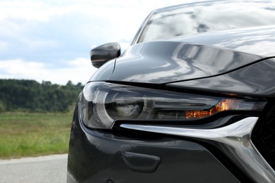 Photo of New black modern car on asphalt road, closeup of headlight