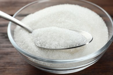 Photo of Granulated sugar in bowl and spoon on wooden table, closeup