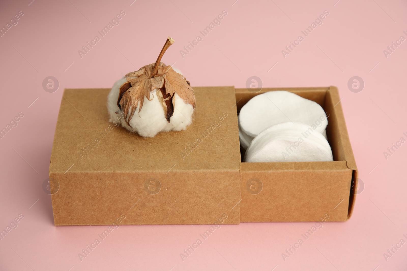 Photo of Cardboard box with cotton pads and flower on pink background, closeup