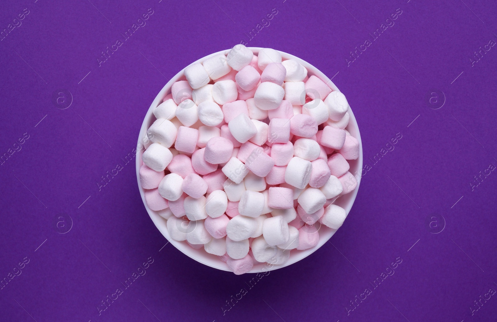 Photo of Bowl with delicious marshmallows on purple background, top view