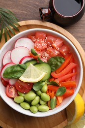 Photo of Poke bowl with salmon, edamame beans and vegetables on wooden table, flat lay