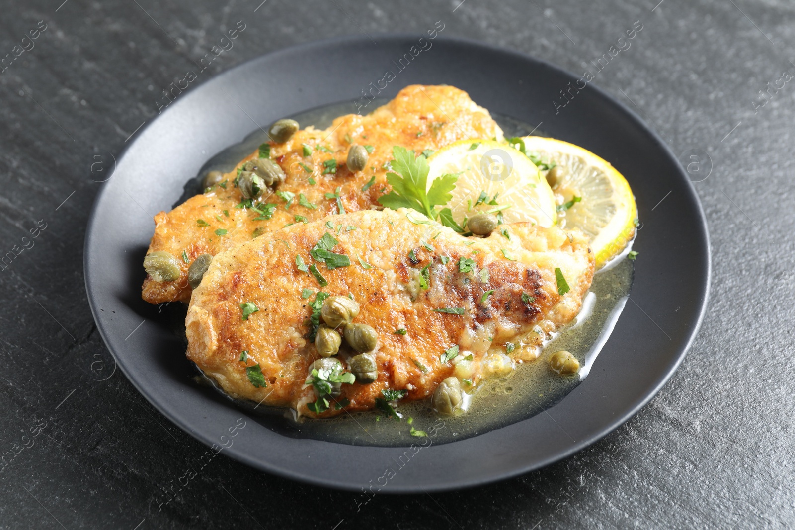 Photo of Delicious chicken piccata with herbs and lemons on black table