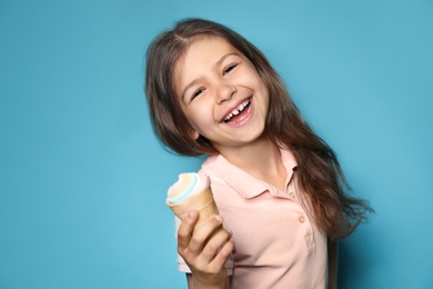 Adorable little girl with delicious ice cream against color background, space for text