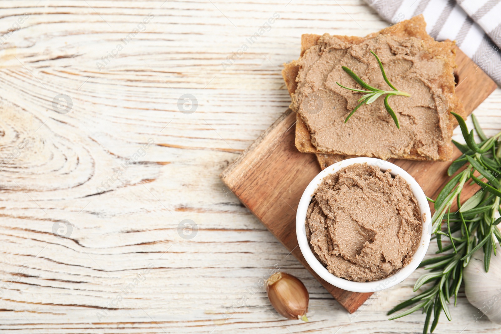 Photo of Crispy crackers with delicious meat pate and rosemary on white wooden table, flat lay. Space for text