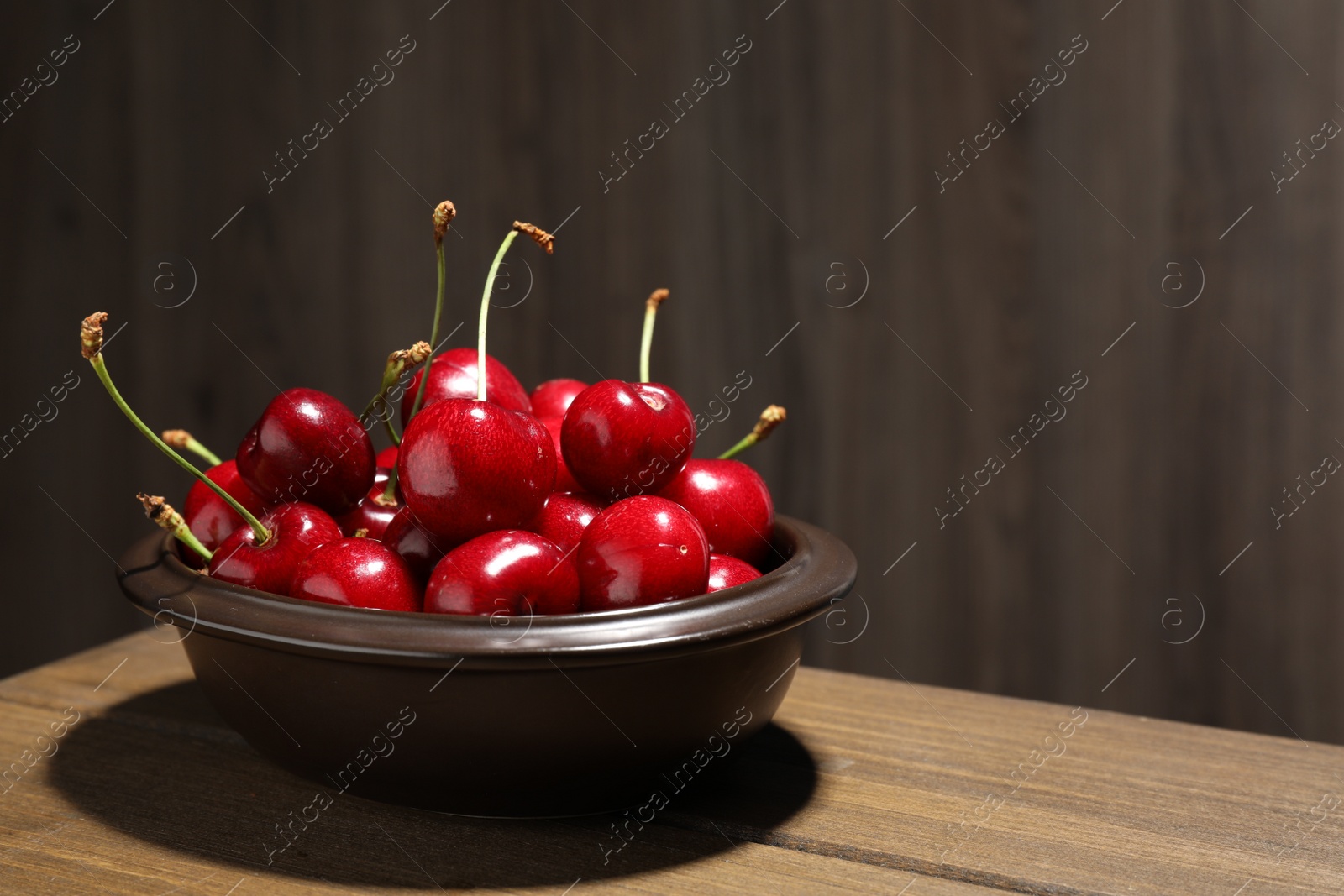 Photo of Sweet red cherries in bowl on wooden table, space for text