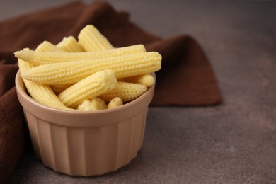 Photo of Tasty fresh yellow baby corns in bowl on brown table, closeup. Space for text