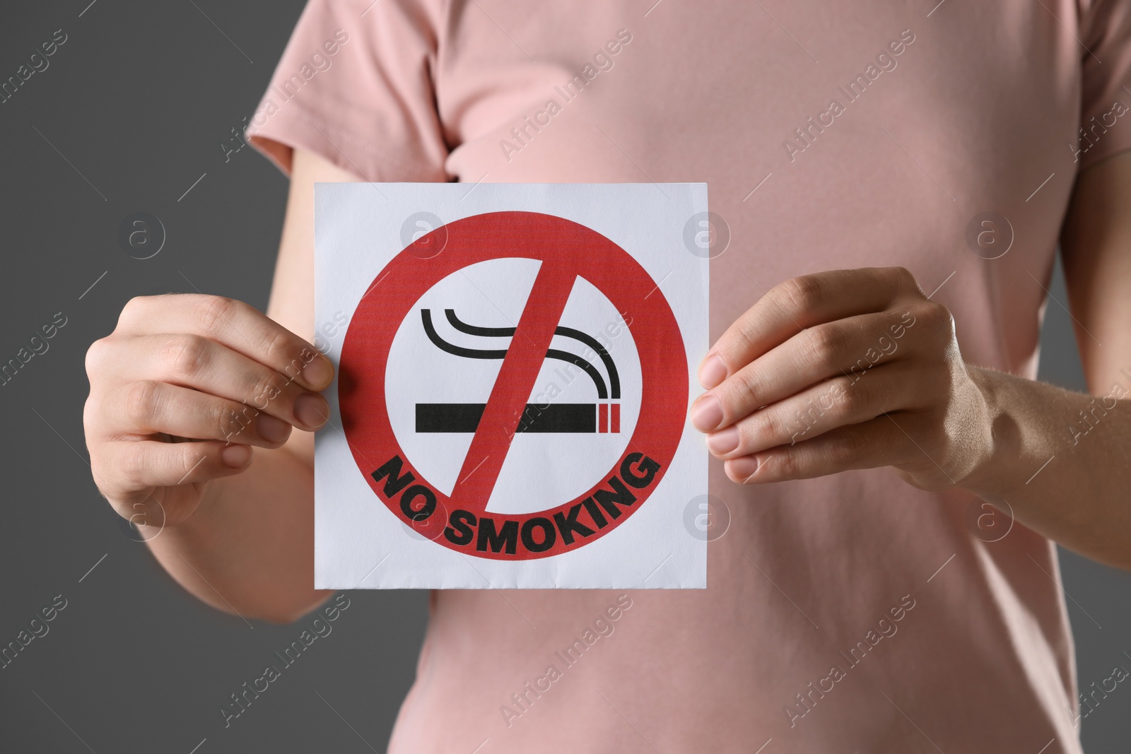 Photo of Woman holding card with no smoking sign on gray background, closeup