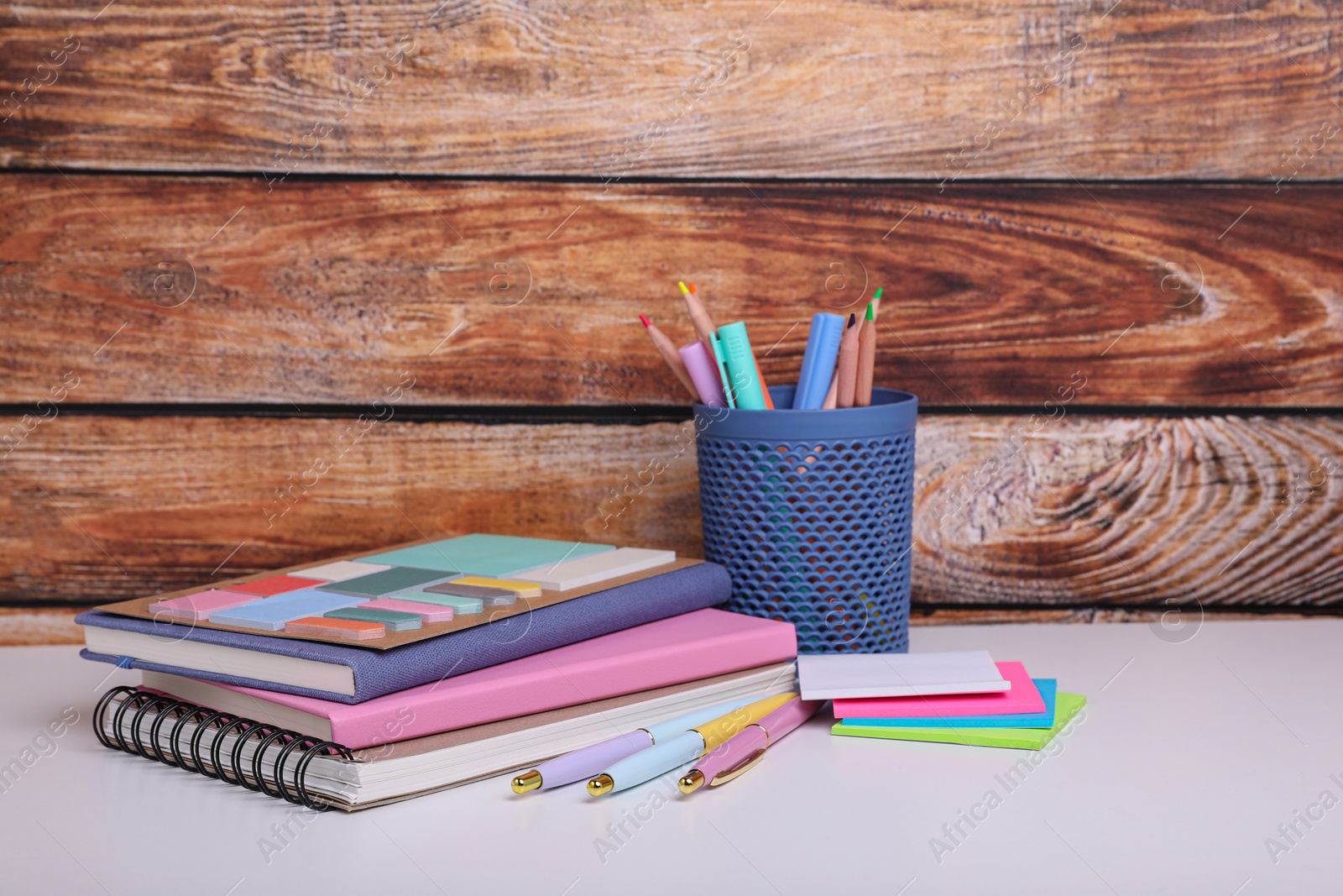 Photo of Different school stationery on white table near wooden wall. Back to school