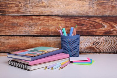 Photo of Different school stationery on white table near wooden wall. Back to school